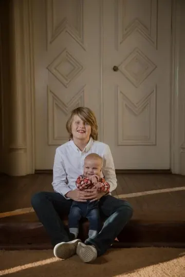 A child and infant sit on a wooden step, illuminated by soft, directional light.