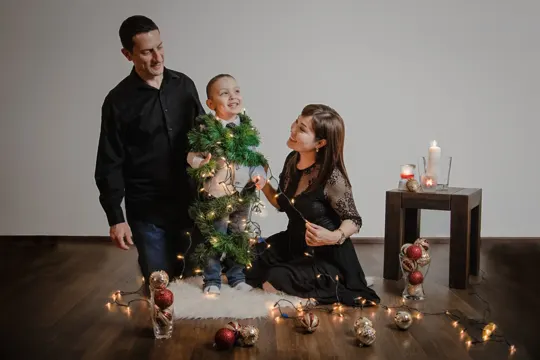 A family gathers amidst Christmas lights and ornaments, with a small table and candles in the background.