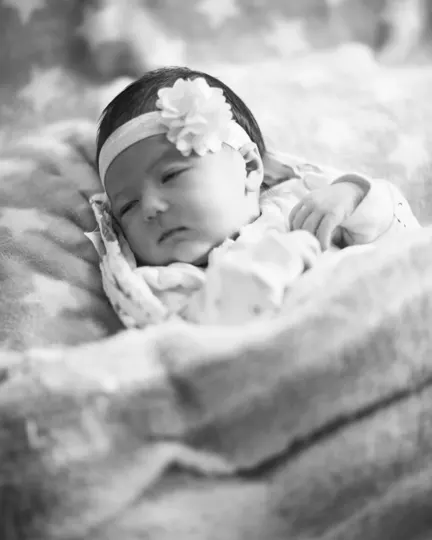 A newborn rests peacefully on a textured blanket, softly lit.