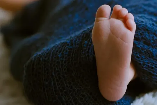 A newborn's foot rests on a textured blue blanket, softly lit.