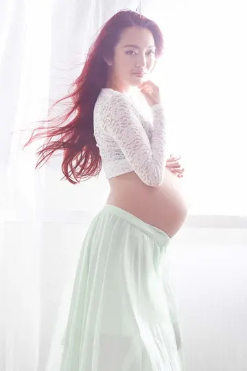 Pregnant woman with flowing red hair, soft white light, and pale green skirt.